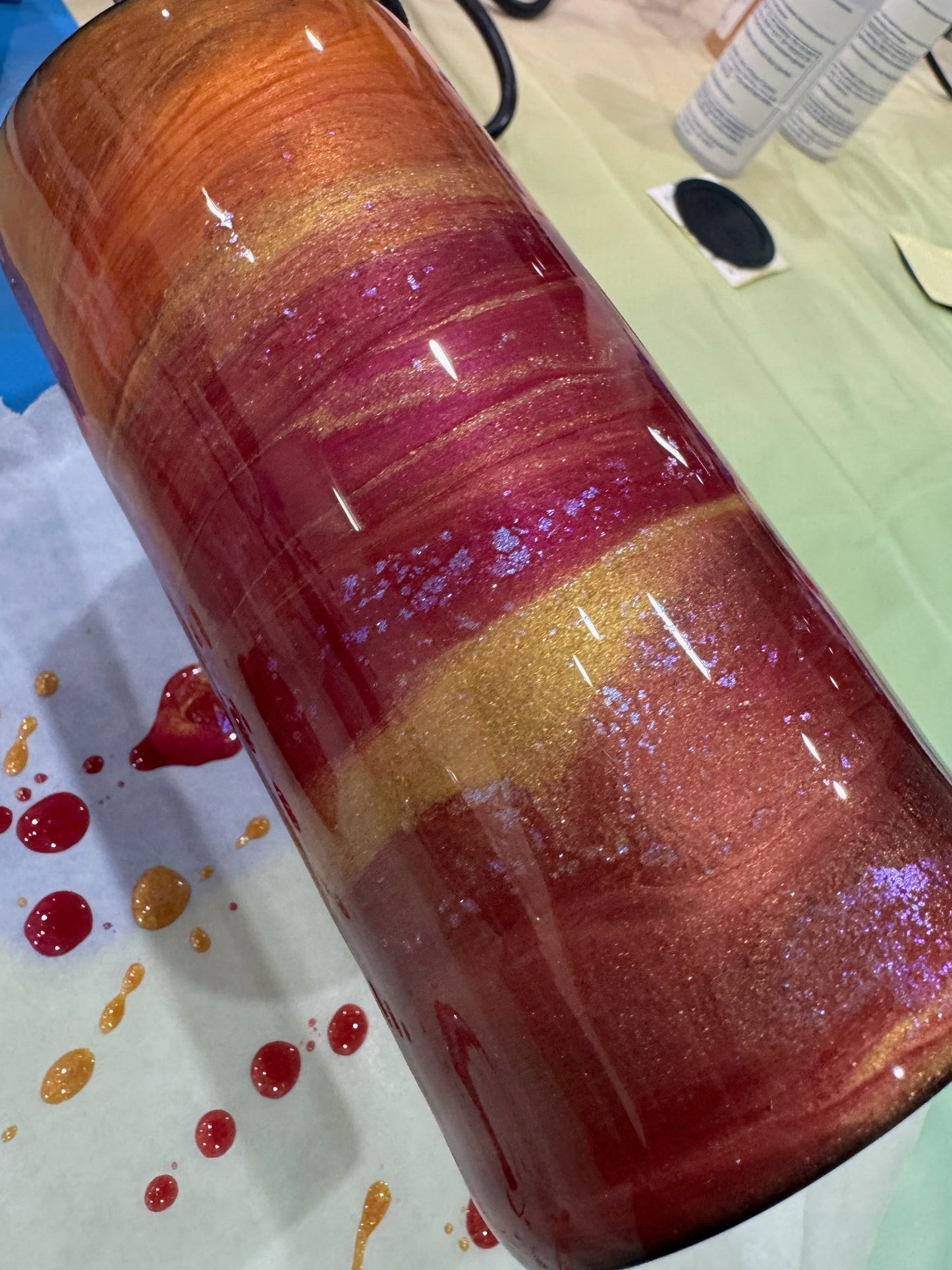 Colorful glass bottle with multicolored pattern on a white surface with paint splashes.