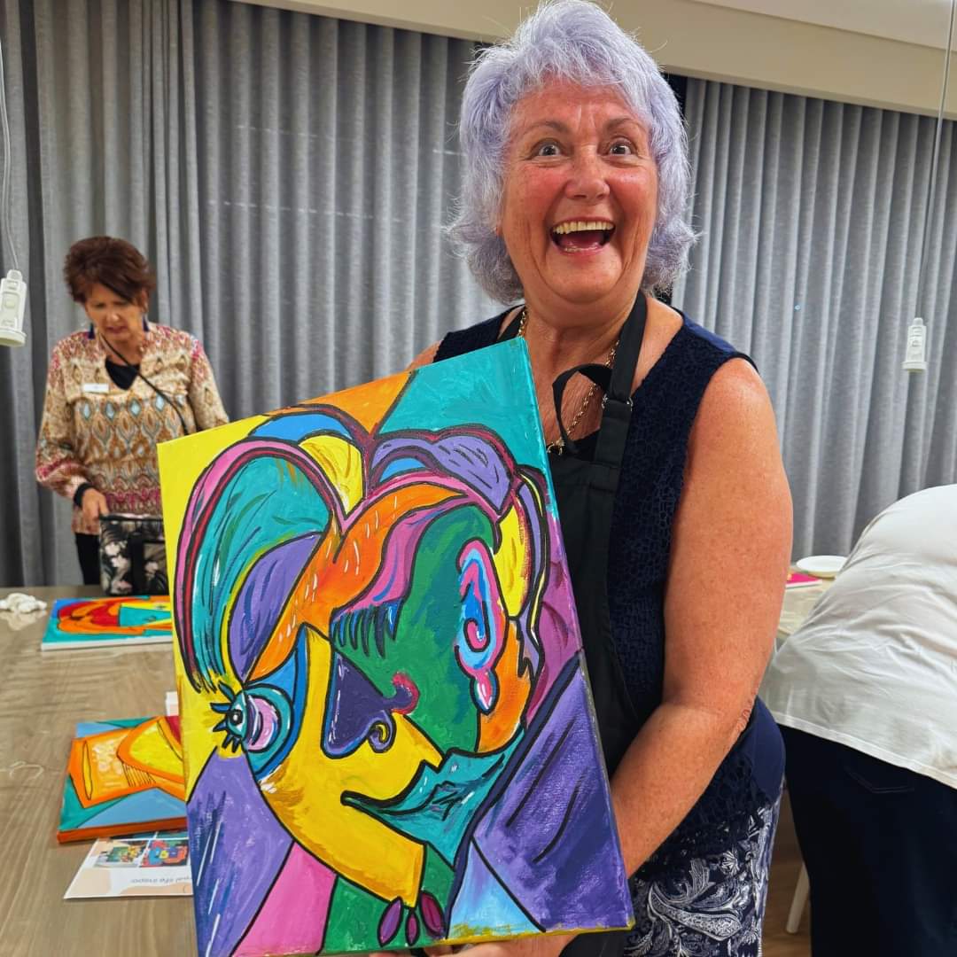 Woman holding a colorful painting in an indoor setting
