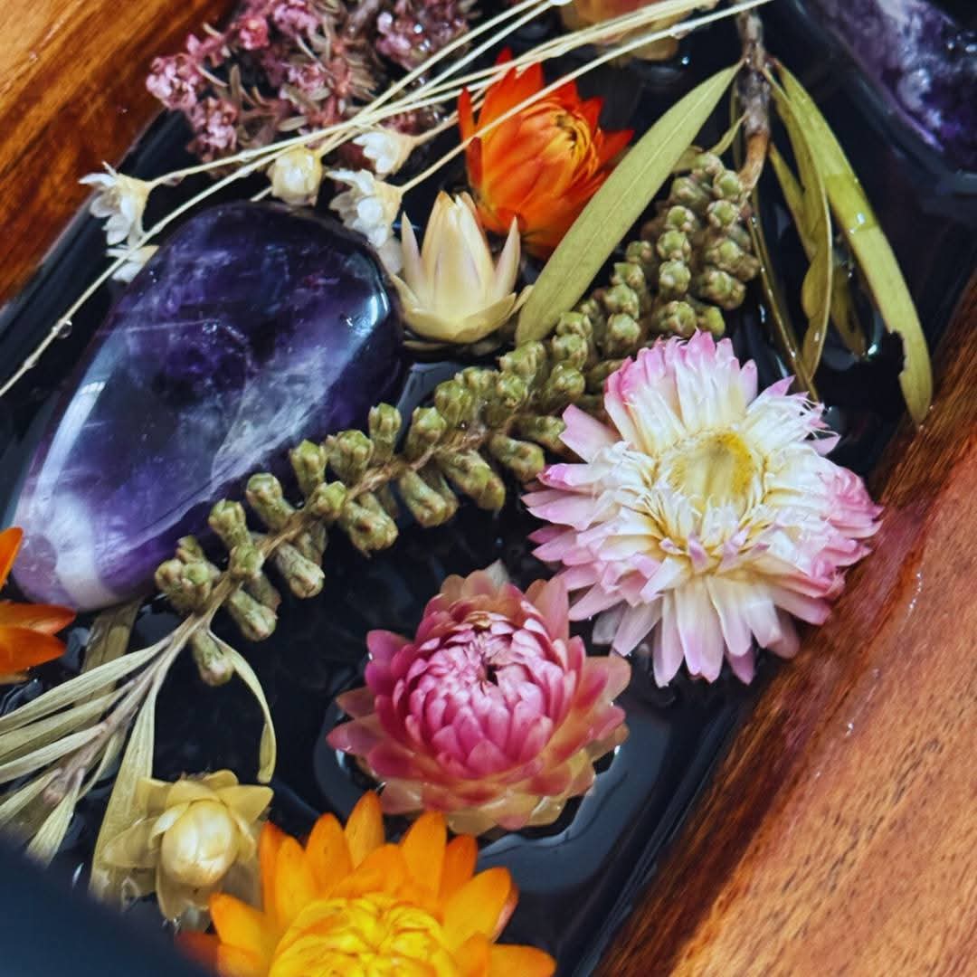 Decorative arrangement of flowers and crystals on a dark surface with a wooden border.